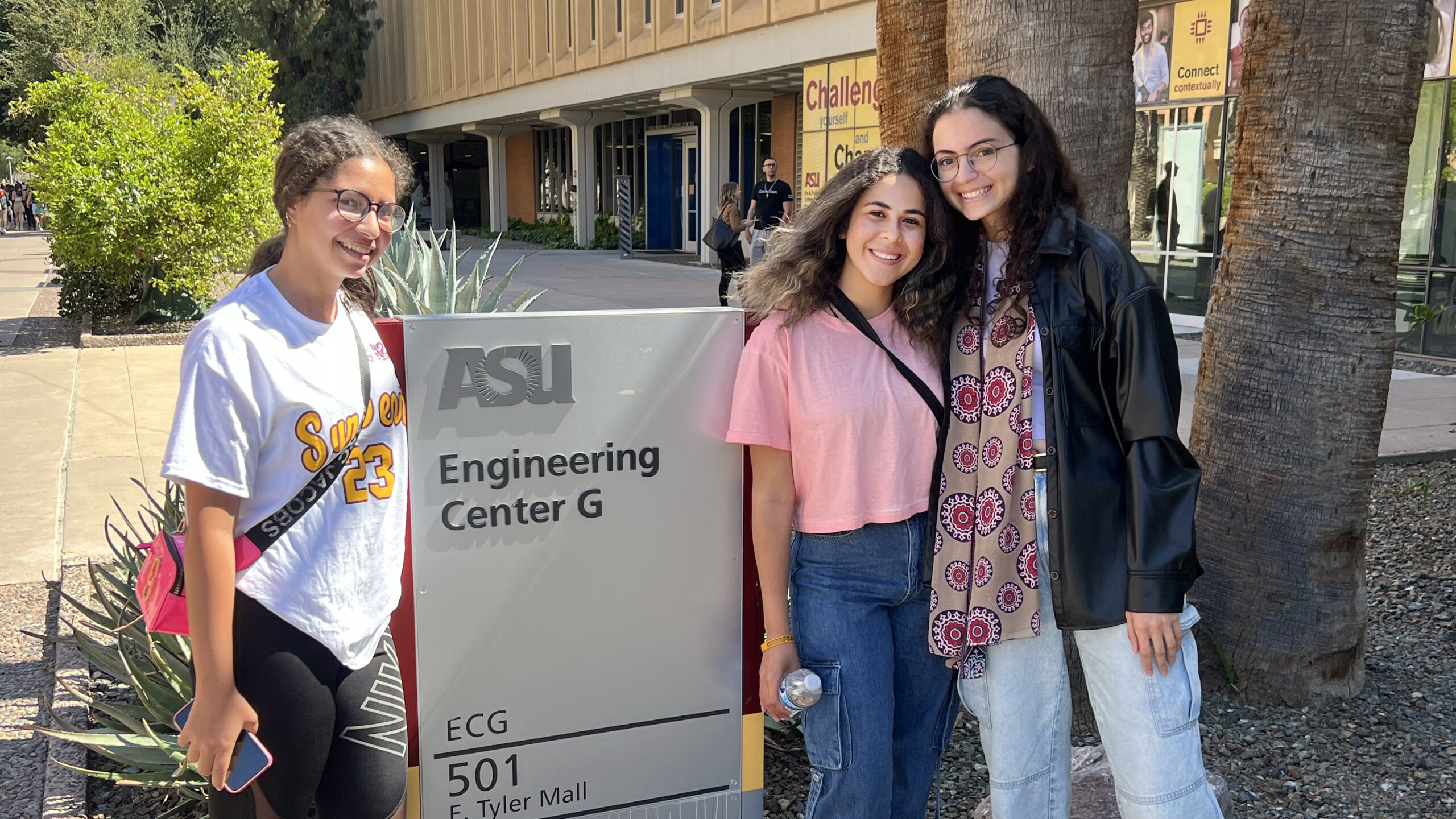 Three young women pose in front of engineering sign