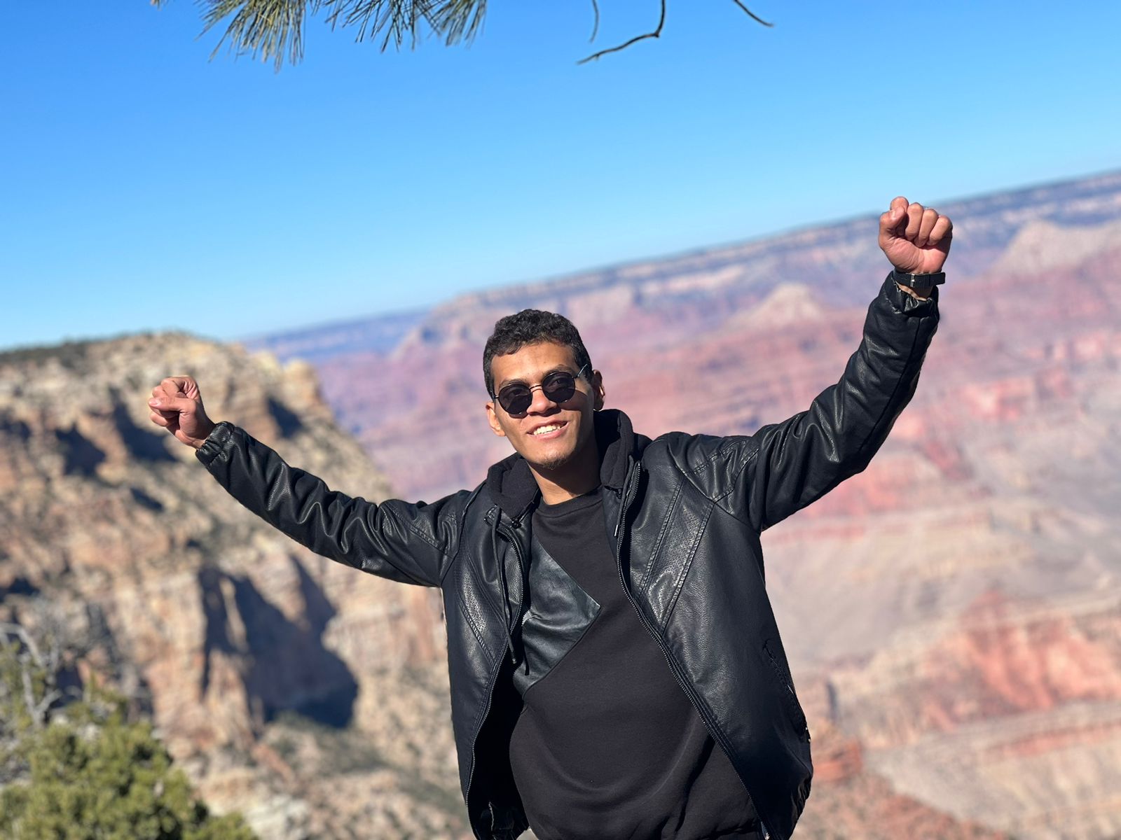 Male exchange student holds arms in the air in celebration in front of the Grand Canyon.